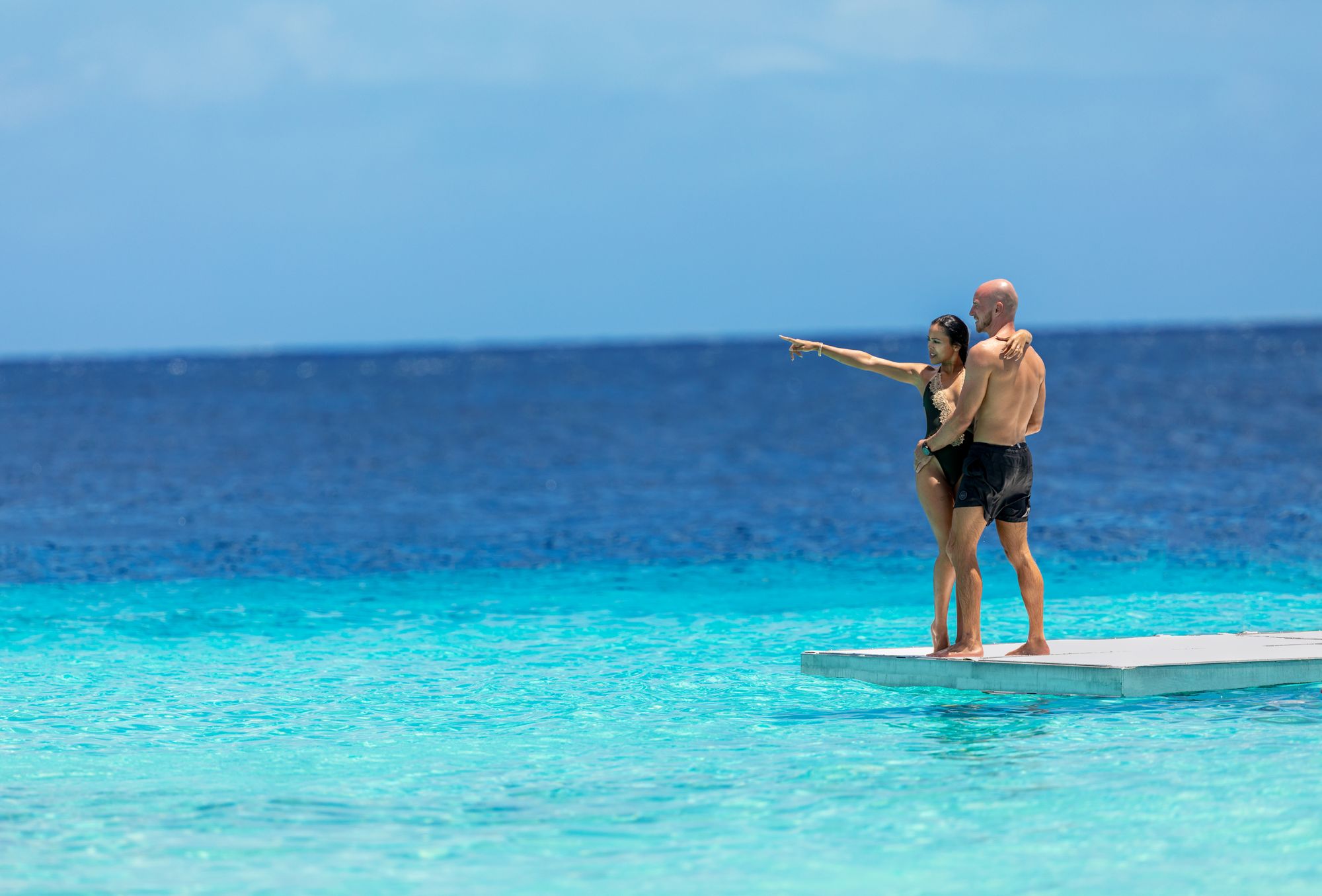 a couple standing on a platform that is surrounded by ocean