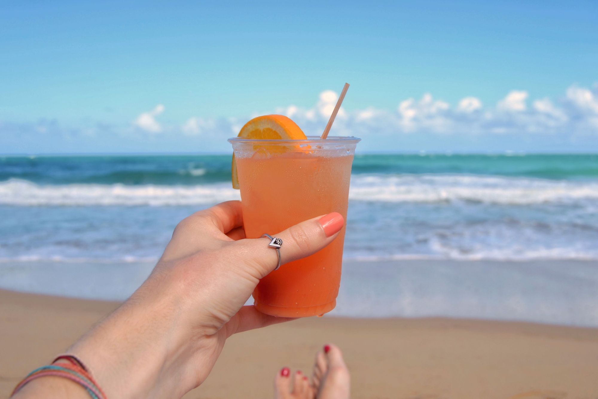 rum punch cocktail held up in front of the beach