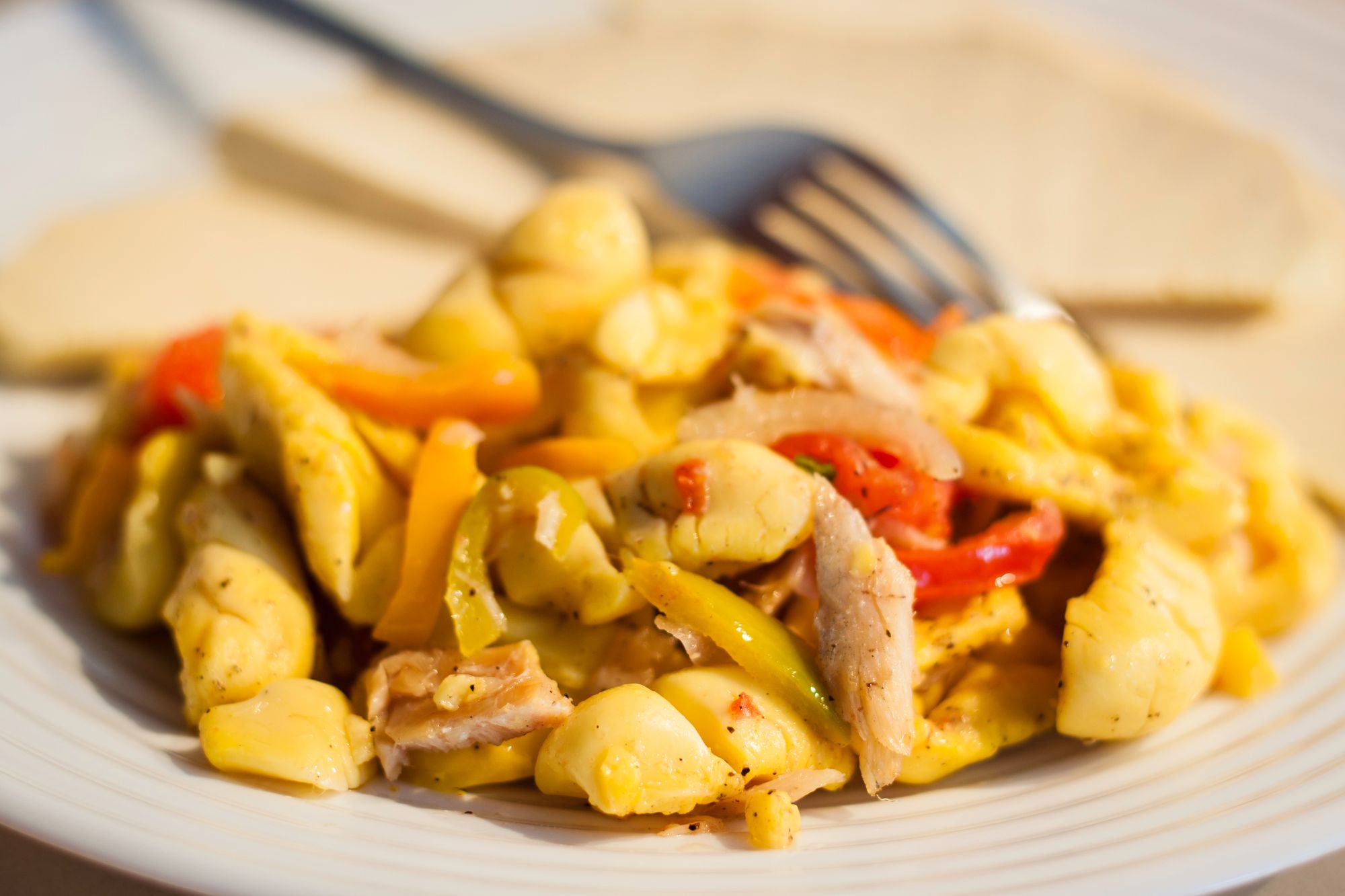 ackee and saltfish on a white plate with a fork in the background out of focus